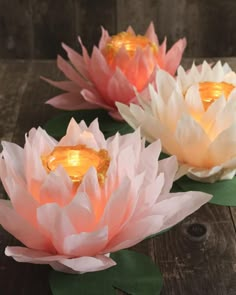 three water lilies sitting on top of a wooden table next to leaves and candles