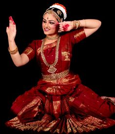 a woman dressed in red and gold sitting on the ground with her hands behind her head