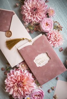 pink flowers and white envelopes with gold tasseling on the inside are laying next to each other