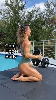 a woman sitting on the ground in front of a swimming pool holding a barbell