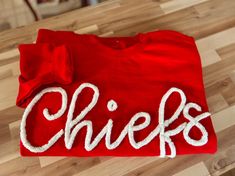 a red shirt with the word chiefs on it sitting on a wooden floor next to a pair of scissors