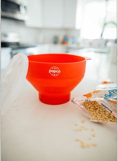 a red bowl sitting on top of a white counter next to a bag of cereal