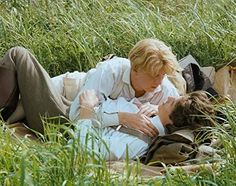 a man and woman laying on the ground in tall grass, one is holding her head