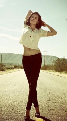 a woman standing on the side of a road wearing black pants and a white shirt