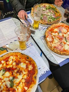 three pizzas are sitting on the table with people eating them and drinking beer in front of them