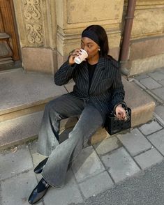 a woman is sitting on the curb drinking from a coffee cup while holding a purse