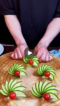 a person cutting cucumbers on top of a wooden board with tomatoes and green leaves