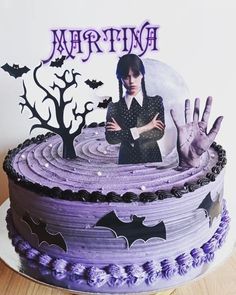 there is a cake decorated with purple icing and bats on the top, along with an image of a woman holding her hand up