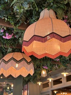 two lamps hanging from the ceiling in front of flowers and greenery at a restaurant