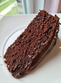 a piece of chocolate cake on a white plate with a window in the back ground