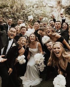 a large group of people posing for a photo with their hands in the air and holding flowers