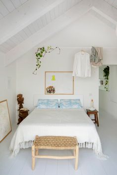 a bedroom with white walls and flooring has a large bed in the corner, along with two wooden stools