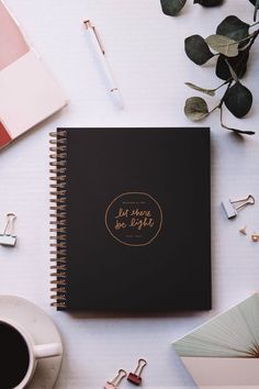 a black notebook sitting on top of a white table next to a cup of coffee