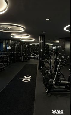 an empty gym with rows of exercise machines and lights on the ceiling, along with black carpeted flooring