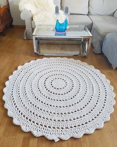 a white crocheted rug sitting on top of a wooden floor next to a couch