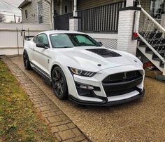 a white mustang parked in front of a house with stairs leading up to the door