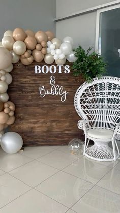 balloons are arranged on the wall behind a white chair and wooden sign that says boots and bubbly