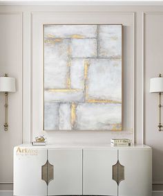 a painting is hanging on the wall above a white cabinet in a room with two lamps