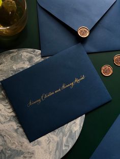 two blue envelopes sitting on top of a marble table next to some gold coins