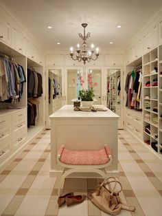 a walk in closet with lots of clothes and handbags on the floor, chandelier hanging from the ceiling