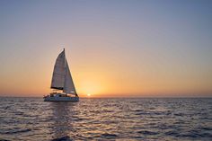 a sailboat sailing in the ocean at sunset