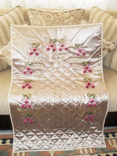 a quilted blanket with pink flowers on it in front of a couch and pillows