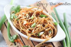 a white bowl filled with noodles and vegetables on top of a wooden cutting board next to green onions