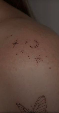 the back of a woman's shoulder with stars and a butterfly tattoo on it