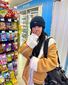 a woman covers her mouth while standing in front of a grocery store display filled with snacks