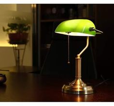 a green table lamp sitting on top of a wooden desk next to a computer mouse