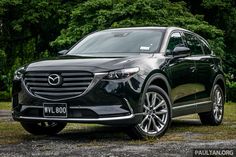 a black mazda cx - 9 is parked in front of some trees and grass