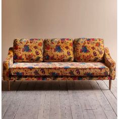 a floral couch sitting on top of a hard wood floor next to a brown wall