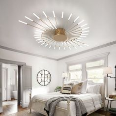 a bedroom with white walls and wood flooring has a circular light fixture above the bed