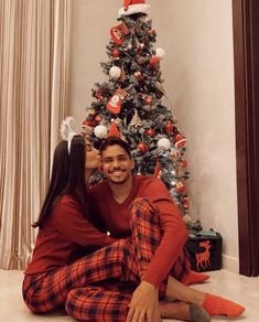 a man and woman sitting in front of a christmas tree