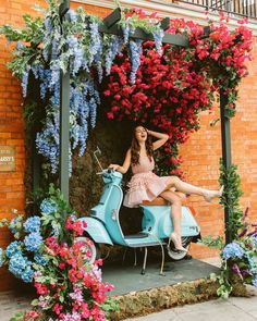 a woman sitting on top of a blue scooter in front of some flowers