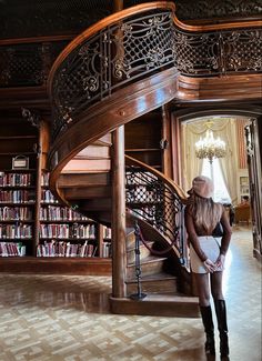 a woman standing in front of a spiral staircase with bookshelves and shelves behind her