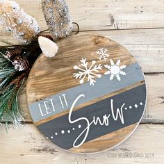 a wooden sign that says let it snow on top of pine cones and evergreen branches