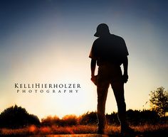 the silhouette of a man standing on top of a dirt field at sunset with trees in the background