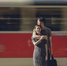 a man and woman standing in front of a train with their arms around each other