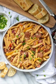 a bowl filled with pasta and meat on top of a table next to some bread