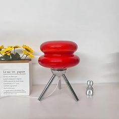 a red stool sitting on top of a table next to a flower pot and a sign