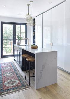 a kitchen with marble counter tops and stools next to an area rug on the floor