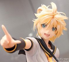 a figurine with blonde hair and blue eyes pointing to the side while wearing a white shirt