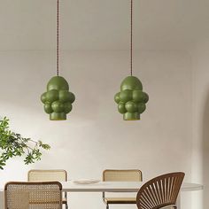 two green lamps hanging from the ceiling above a table with chairs and a potted plant