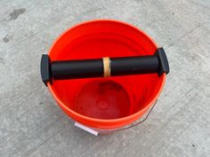 an orange bucket with a black handle on the floor next to a red bowl and white tag