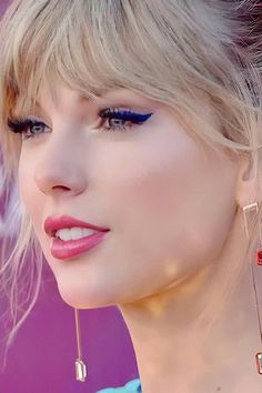 a close up of a person with blue eyes and blonde hair wearing gold ear rings