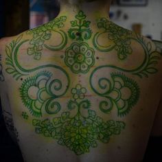 the back of a woman's body with green and white tattoos on it,