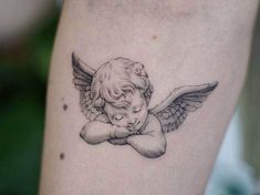 an angel tattoo on the leg of a woman's arm with her head resting on her chest