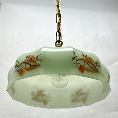 a glass light hanging from a chain on a white wall with flowers painted on it