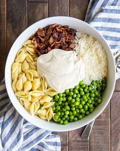 a white bowl filled with pasta, peas and bacon on top of a wooden table